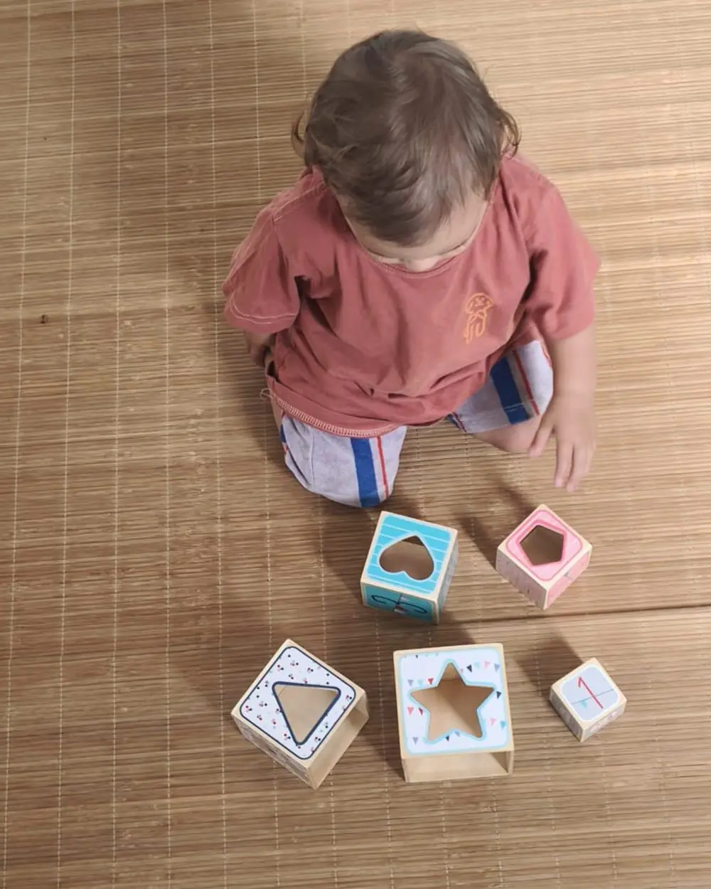Jeune enfant en jeu libre au sol avec des cubes de formes, vue de dessus