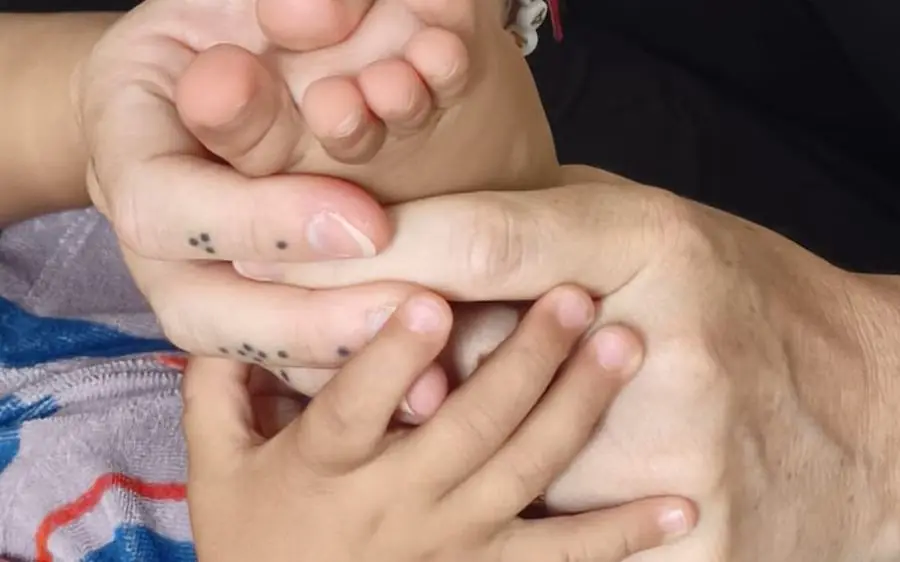 Mains d'adulte accompagnant le pied et la main d'un jeune enfant