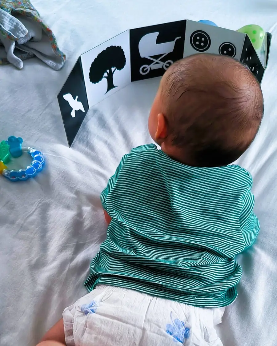 Bébé sur le ventre en motricité libre, redressé sur ses avant-bras devant un livre d'éveil contrasté